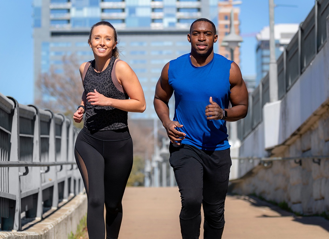 Employee Benefits - Man and Woman Jog Together on a Bridge Path on a Sunny Day